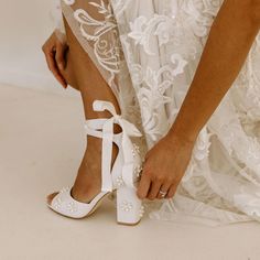 a woman in white shoes tying her shoelaces on top of her wedding dress