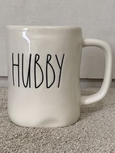 a white coffee mug with the word hubby written on it sitting on a carpeted floor