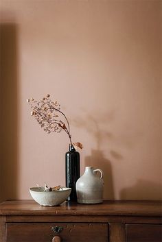 two vases and a bowl sit on a dresser in front of a pink wall