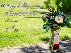 a vase filled with flowers sitting on top of a brick walkway next to a grass covered field