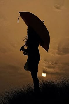 the silhouette of a woman holding an umbrella in front of a sunset with clouds and grass