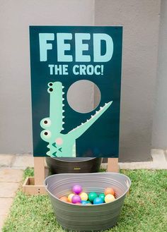 a sign that says feed the croc and some eggs in a bucket on grass