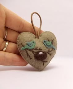 a hand holding a heart shaped ornament with two birds on it