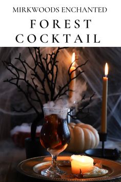 a table topped with a glass filled with liquid next to a candle and some pumpkins