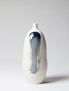 a white vase with blue and black designs on the bottom, sitting in front of a gray background