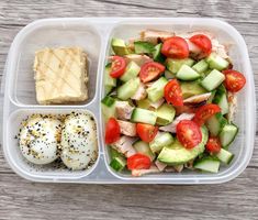 a plastic container filled with food on top of a wooden table next to a piece of bread