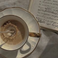 an open book is next to a teacup and saucer with liquid in it