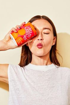 a woman holding a can of orange juice to her face and drinking it from a cup