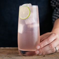 a person holding a drink with a lime slice in it's glass on a wooden table