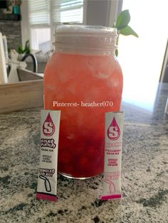 a pink drink sitting on top of a counter next to a bottle of liquid and two tags