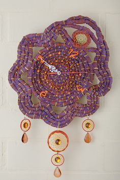 a purple and orange clock hanging from the side of a brick wall with beads on it