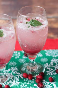 two glasses filled with ice and cranberries on top of a green table cloth