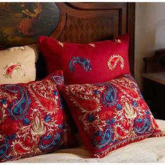 two red pillows sitting on top of a bed next to each other in front of a painting