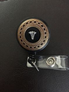 "🔸🔸orders are delayed by a few days this week. Thank you for your patience Nurse gift, nurse retractable badge holder badge clip This badge id holder has an antiqued bronze stamping attached and adorned with the Caduceus symbol. This badge reel has a retractable cord, a swivel 360 degree rotation alligator spring clip, a nonswivel belt clip, or a belt clip with loop which can attach to a lanyard or necklace, and a clear vinyl strap with your choice of charm attached- either syringe with contai Black Retractable Badge Holders As Gift, Black Retractable Badge Reel For Gift, Black Badge Reel With Swivel Clip As A Gift, Caduceus Symbol, Retractable Badge Holder, Nurse Badge Reel, Name Badges, Nurse Badge, Retractable Badge Reel