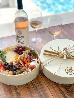 a wine bottle and some food on a table next to a bowl with grapes in it