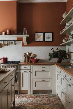 a kitchen with an orange wall and white cabinetry is seen in this image, there are many dishes on the counter