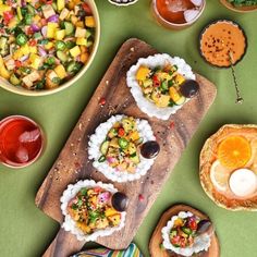 an assortment of food is displayed on a wooden cutting board with bowls and spoons