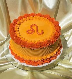 an orange and yellow cake with the letter s on it sitting on a glass plate