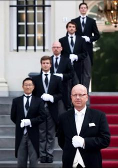 a group of men in black suits and white gloves standing on steps with their arms crossed