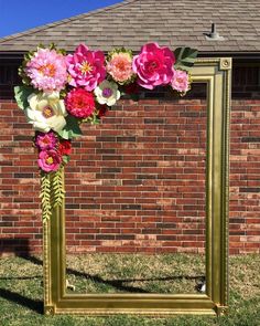 a gold frame with pink and white flowers on it in front of a brick wall