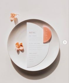 a white plate topped with a piece of paper next to a flower on top of it