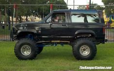 a large black truck parked on top of a lush green field next to a metal fence