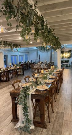 a long table set up with place settings and greenery hanging from the rafters