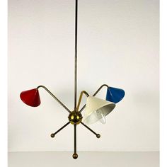 three colored lamps are hanging from a metal pole on a white wall background, one is red and the other is blue