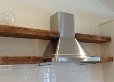 a stainless steel range hood mounted on a wooden shelf above a white tiled kitchen counter