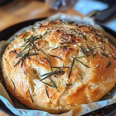 a loaf of bread with rosemary sprigs on top sits in a black pan