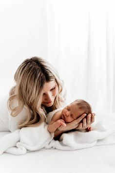 a woman holding a baby wrapped in a white blanket on top of a bed covered in blankets