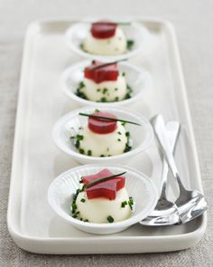 four small white plates filled with food on top of a table next to utensils