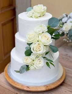 a three tiered white wedding cake with flowers on the top and greenery at the bottom