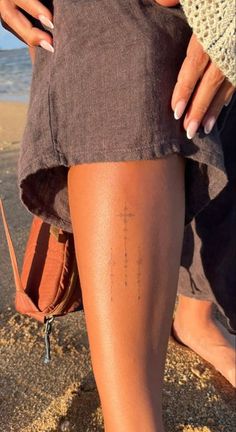 a woman's legs with small tattoos on them and her purse in the sand