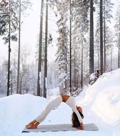 a woman doing yoga in the snow with her arms and legs bent over her head