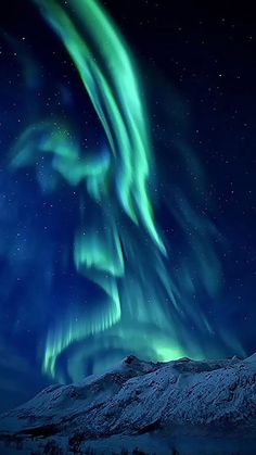 an aurora bore is seen in the night sky above snow covered mountains and trees, with bright green lights