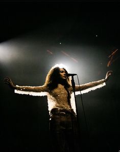 a woman standing in front of a microphone with her arms spread out and hands outstretched