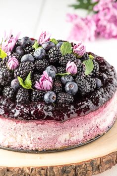 a cake with blueberries and blackberries on top sitting on a wooden board next to flowers