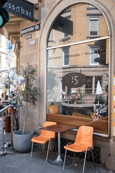 two orange chairs sitting in front of a window on the side of a building next to a potted plant