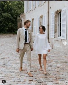 a man and woman walking down a cobblestone street holding hands, smiling at each other