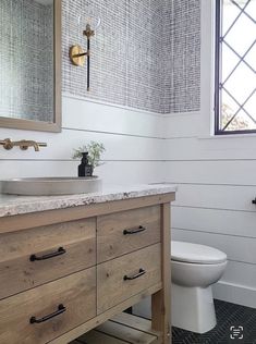 a white toilet sitting next to a bathroom sink under a mirror on top of a wooden cabinet