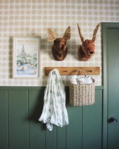 two deer heads mounted to the side of a wall next to a basket and coat rack