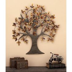 a metal tree with leaves on it sitting next to a trunk and suitcase in front of a wall