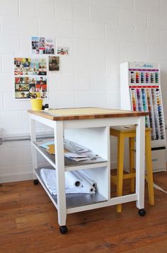 a white table with yellow legs and a magazine rack on the top, in front of a brick wall