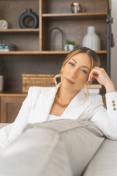 a woman in a white suit sitting on a couch with her hand under her head