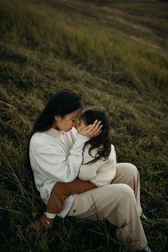 two women are sitting in the grass and one is holding her face to her chest