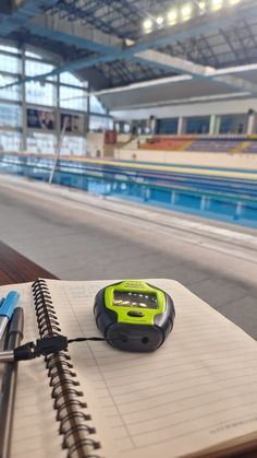 a notebook with a pen and an electronic device on top of it next to a swimming pool