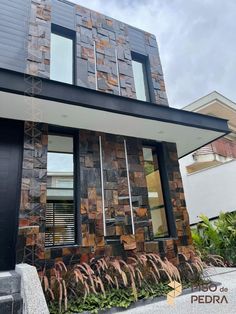 a modern house made out of wood and stone with plants in the front garden area