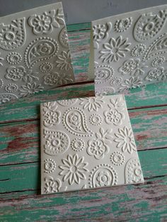 two white tiles sitting on top of a wooden table next to each other and one has an intricate design