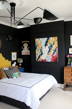 a bedroom with black walls, white bedding and colorful artwork on the wall above it